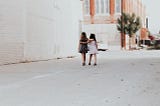 two little girls holding each other and walking