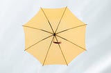 Foto de um guarda-chuva amarelo aberto em um céu nublado.