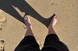Mark’s bare feet on sand, casting a shadow to the left