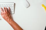 fingers typing on keyboard, a mouse and a yellow watch strap