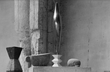 Black and White photo of the 1926 Sculpture “Bird in Space” on a plinthy with some abstrtact objects beneath.