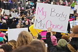 A group of people in a protest, including one woman holding a sign that says “My Body My Choice”