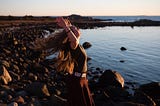 Woman standing by the ocean with her arms open to the sky.