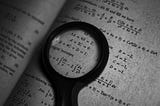 A magnifying glass zooming in on a math formula of a book.