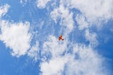 Red airplane viewed from far below against a blue sky with white clouds.