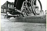 Mid-century photo of person in wheelchair navigating inaccessible sidewalk.