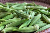 Fresh okra pods are spread on a brown basket.