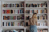 Lady standing at a library bookshelf looking at a book she is curious about