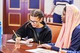 Two students write on paper while sitting at a table.