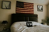 flag above bed headboard, laptop on bedsheets showing 8:45