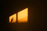 A raised palm and window reflected by the rays of the sun on a wall.