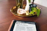 Ereader on a kitchen table, the screen is on and showing a report. In the background a crystal, candle, vase and a plant can be seen.