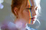 A young woman’s profile with a prism of rainbow light shining on her face.