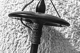 A wooden top-whirl drop spindle with yarn wound around it. It’s in black-and-white because it looked more artsy that way