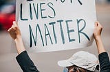 Masked white woman holding up a “Black Lives Matter” sign