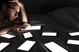 A man in a dark room with nine electronic tablets on a black desk in front of him