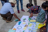 A man and two women kneel over a large piece of paper covered in images and notes as part of preparation for community diagnostics, Panicuy y Calbalcol, Guatemala.