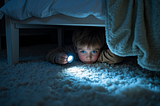 Child with a flashlight searching under a bed for Christmas presents.