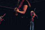 Viola player wearing black is on a dark stage with moody lighting. There are two other viola players in the background out of focus