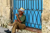 Cuban man smokes cigar on a step in front of a distinctive sky blue doorway