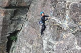 A woman rock climbing. She’s smiling and wearing a helmet