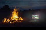 A bonfire burns at night, with a TV glowing beside it. A still from the ‘our stories’ TV ad by Uncommon Studios.