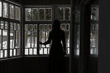 Pensive female standing and looking at window in dark room.