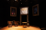 A theatrical set with wooden chairs, wooden floor, and a banner that reads “The Fantastic Francis Hardy, Faith Healer, One Night Only”