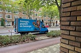 This is a picture of a blue delivery truck with a picture of fresh food on it and Dutch words that say, “Geoogst, geplukt en bezorgd,” which means, “harvested, picked and delivered.”