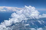 A view from an airplane window of fluffy clouds, blue sky, and land below.