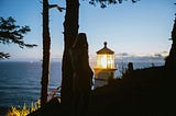 A photo of the silhouette of a woman beside a tree overlooking the top of a lighthouse beside the ocean