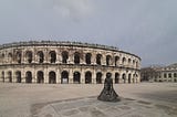 The ancient Roman arena of Nimes, France, with a statue of a matador spreading his cape outside.