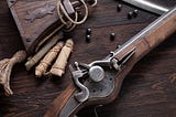 17th century ancient flintlock musket with powder flask and led bullets on wooden deck.