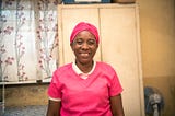 Malagasy midwife Anasthasie, dressed in pink scrubs and headscarf, smiles for the camera.