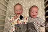 Joshua and Caleb laying side by side smiling at home in a crib