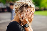 girl with blonde hair in braids around her head holding her hands over her face