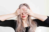 A woman covers her eyes gesturing “See no Evil”