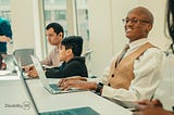 Smiling man with a learning disability works on a laptop in a meeting with other colleagues.