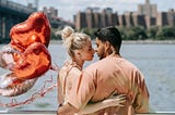 Young woman holding heart-shaped balloons kissing her boyfriend