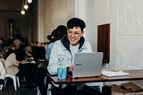 Woman sitting in front of an open laptop in a café, smiling