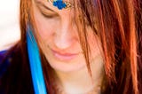 Young red-haired woman dressed in blue, looking down in contemplation.