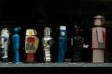 A variety of toy robots stand on a shelf.