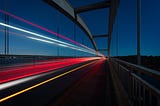 Bright lines of light accelerate across a bridge at night.