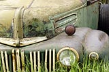 Front end of rusty vintage Ford truck sitting in a patch of weeds.