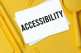 A yellow desk with several yellow elements like a magnifying glass, two pencils, a paper clips and right in the center, a white paper card written accessibility