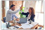 Professional colleagues high-fiving at a desk