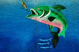 Mural of a green fish about to bite onto a lure against a bright blue wall