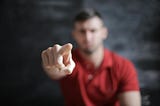 A man pointing at the camera. The man’s face and body are out of focus, but his finger pointing at you is perfectly in focus.