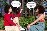 Two women are sitting outside on a sunny day, engaging in conversation. One is wearing a red sweater with a colorful pattern on the front, light-colored pants, and white shoes, and has sunglasses on. The other is dressed in a green jumpsuit with a red top underneath. They’re surrounded by greenery and a modern building in the background. Speech bubbles show them talking: one asks “How’s it going?” and the other replies, “Ok. Except for my husband’s rash!”