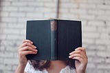 Woman reading a book — face obscured by the book